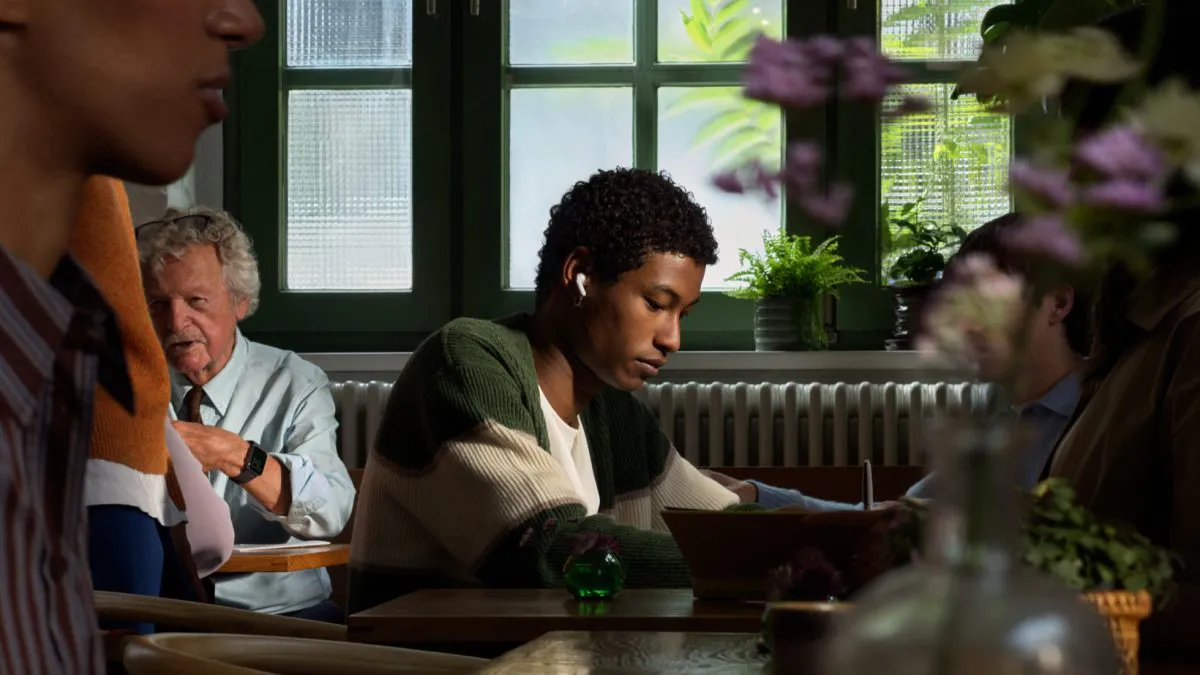 Una persona che indossa gli AirPods 5 mentre lavora al ristorante circondata da altre persone.