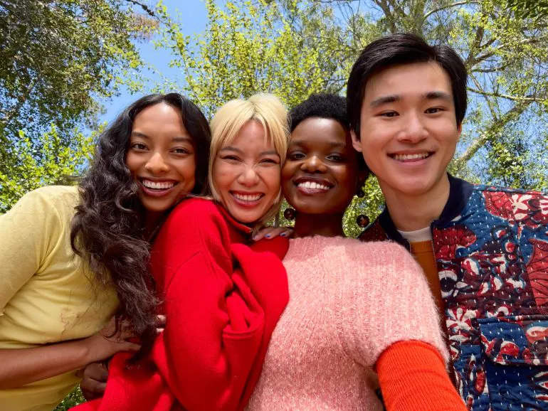 Quattro persone sorridono e si mettono in posa per un selfie all’aperto